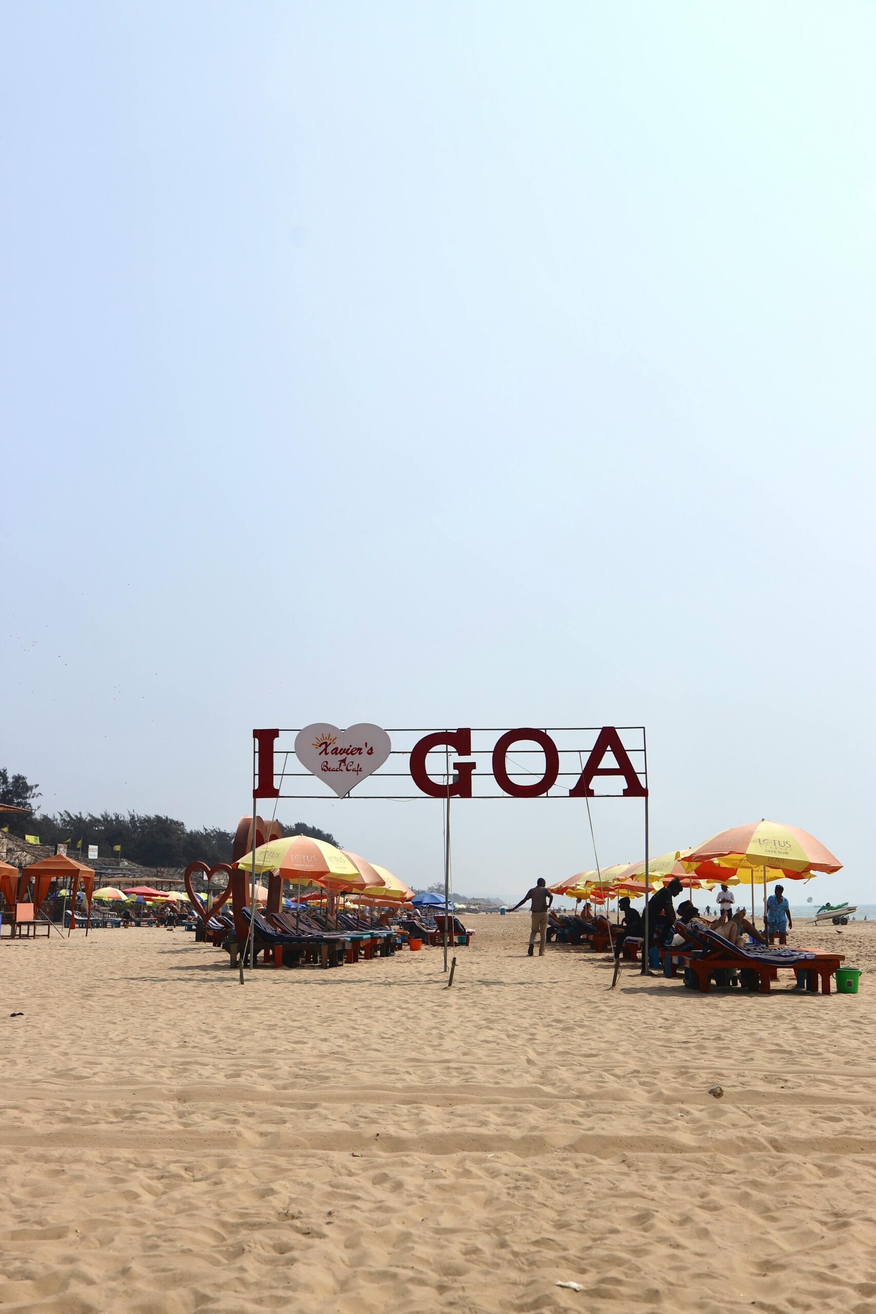 Home Relaxing beach scene in Goa, India, featuring colorful umbrellas and a sign reading
