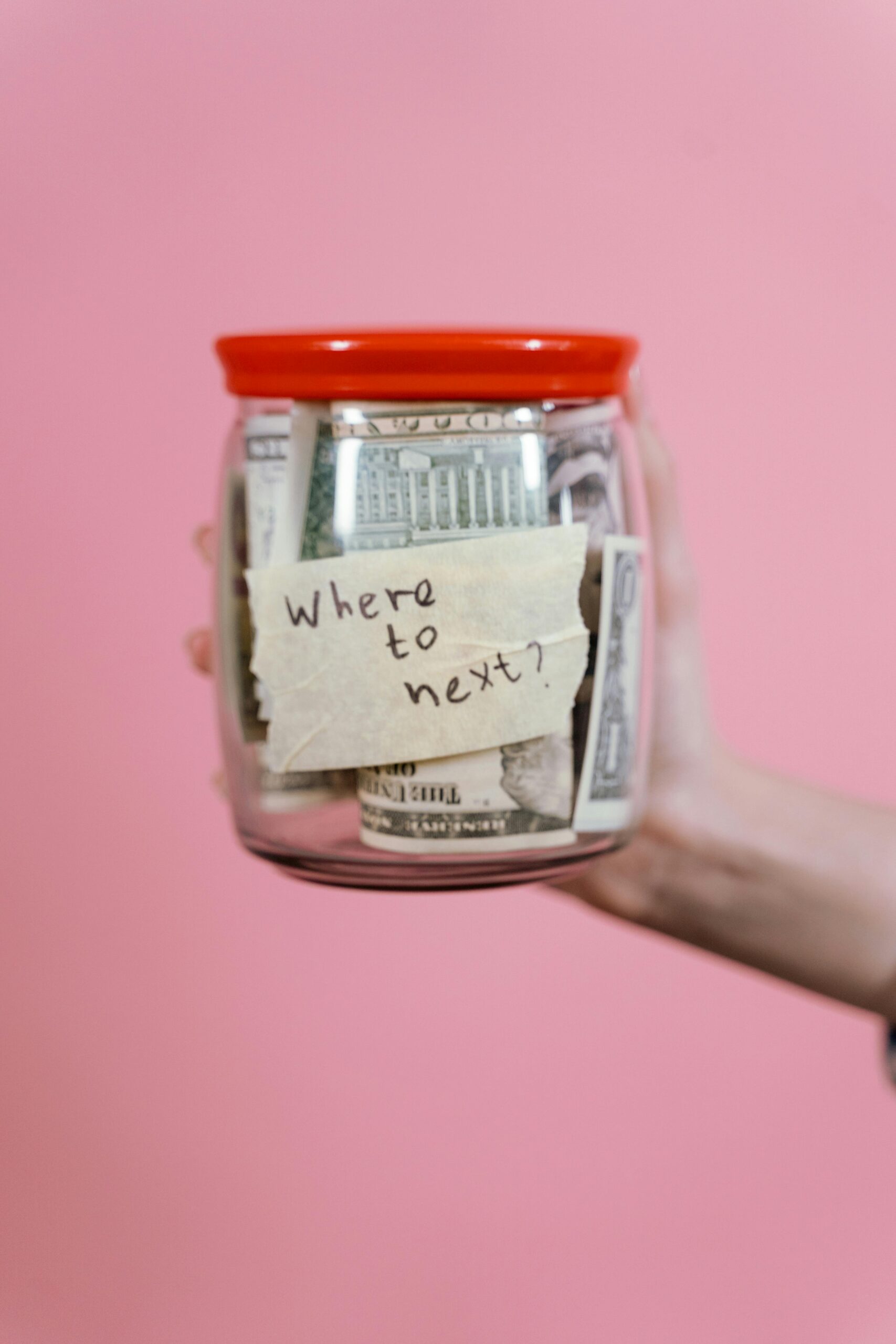 Home A jar filled with cash and a travel note against a pink backdrop symbolizing savings.