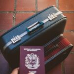 A traveler's essentials including a passport and suitcase on a red tiled floor, suggesting a journey ahead.