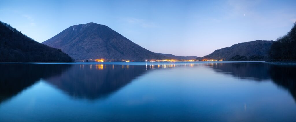 Best Places to Visit in Japan in 2026: 25 Amazing Must-See Gems Beautiful night view of Lake Chuzenji with Mount Nantai in Nikko, Japan reflecting lights over water.