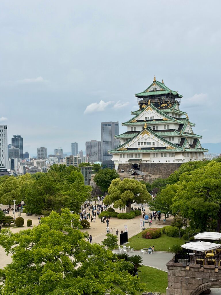 Best Places to Visit in Japan in 2026: 25 Amazing Must-See Gems Scenic view of Osaka Castle surrounded by lush greenery and urban skyline on a cloudy spring day.